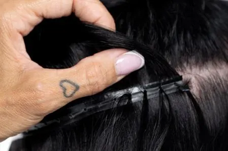 Finger teilen dunkles Haar, darunter die mit feinen Microringen befestigte Weft